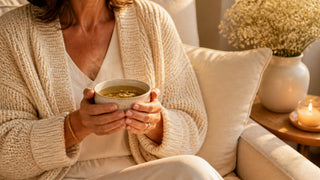 Femme en gilet beige tenant une tasse de tisane, moment cocooning